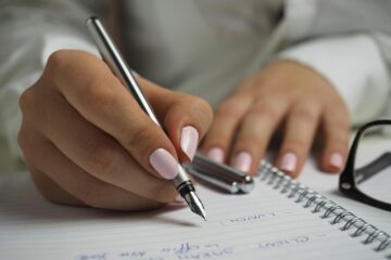 A detailed image of handwriting in a notebook with a fountain pen and glasses, ideal for office themes.